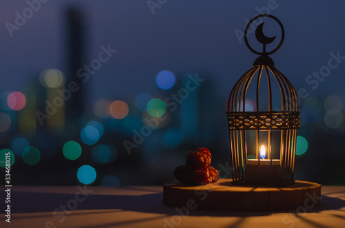 Lantern that have moon symbol on top and dates fruit put on wooden tray with colorful city bokeh lights for the Muslim feast of the holy month of Ramadan Kareem.