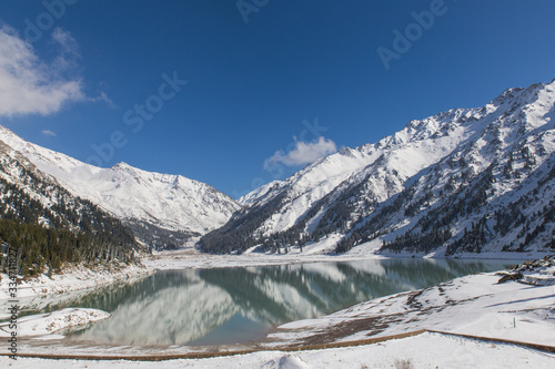 mountain big almaty lake with snow covered hills and trees in may near Almaty, Kazakhstan