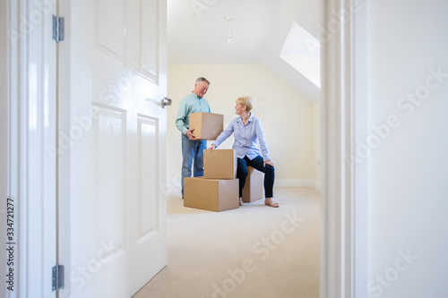 Senior Couple Downsizing In Retirement Carrying Boxes Into New Home On Moving Day