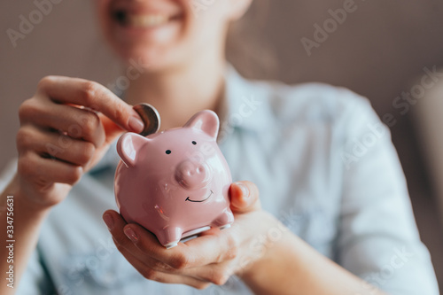 female hands hold a pink piggy bank and puts a coin there. The concept of saving money or savings, investment