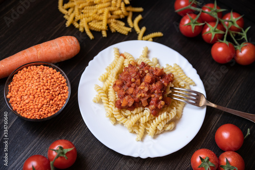 Makaroni mit veganer Nudelsoße a la Bolognese aus roten Linsen, Tomaten und Möhren auf schwarzen Untergrund aus Holz