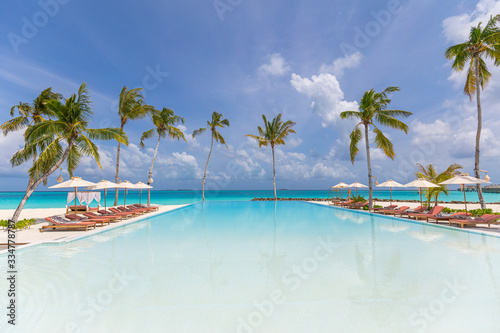 Outdoor tourism landscape. Luxurious beach resort with swimming pool and beach chairs or loungers under umbrellas with palm trees and blue sky. Summer travel and vacation background concept 