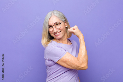senior or middle age pretty woman feeling happy, satisfied and powerful, flexing fit and muscular biceps, looking strong after the gym