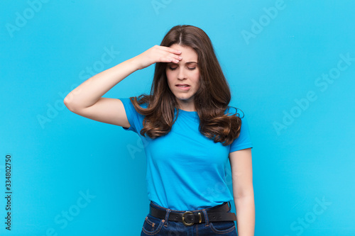 young pretty woman looking stressed, tired and frustrated, drying sweat off forehead, feeling hopeless and exhausted against blue wall