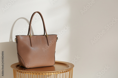 Stylish leather woman's bag on table near light wall. Space for text