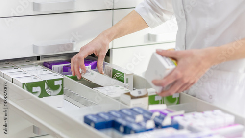 Pharmacist holding medicine box and capsule pack in pharmacy drugstore.