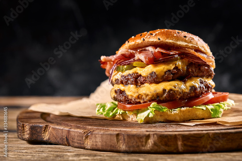 Juicy American burger, hamburger or cheeseburger with two beef patties, with sauce and basked on a black background. Concept of American fast food. Copy space