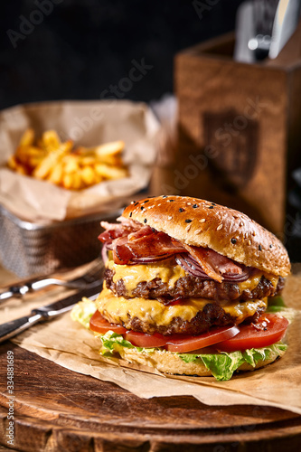 Juicy American burger, hamburger or cheeseburger with two beef patties, with sauce and basked on a black background. Concept of American fast food. Copy space