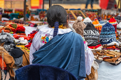 Indigenous women in traditional clothing and hairstyle by her market stall on the sunday art and craft market of Otavalo, North of Quito, Ecuador.