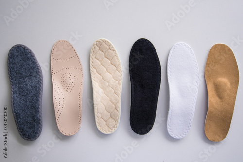 Studio photo of orthopedic insoles. A variety of orthopedic insoles are laid out in a row. Different colors and coatings: leather, cotton, microfiber.