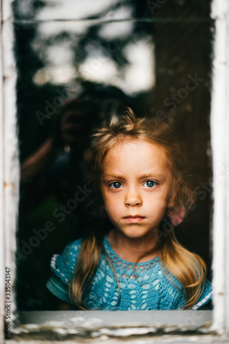 Lonely abandoned unhappy little girl looking through window with abstract reflections. Kid depressive portrait. Pathetic sad misery child eyes. Problematic childhood. Deep mood. Pensive baby face.