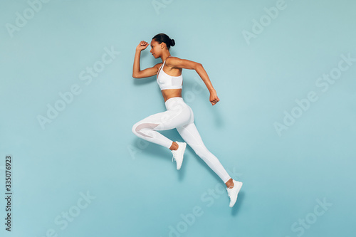 Sports woman running in studio. Full length shot of young female exercising over blue backgroud.