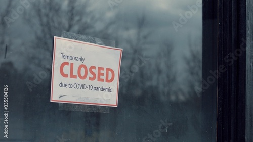 FIXED view of a Temporary closed due COVID-19 pandemic sign hanging on a window. Coronavirus pandemic, small business shutdown