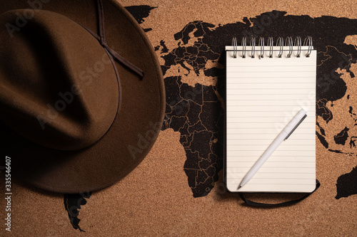 Zdjęcie kapelusza i notesu z długopisem na tle mapy świata