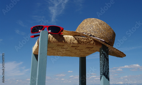 Sombrero y gafas de sol sobre taburete y cielo azul de verano