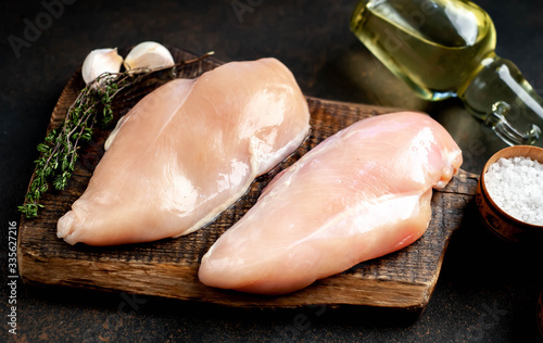 raw chicken breast on a cutting board with spices and a meat knife on a stone background