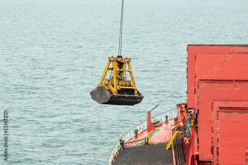 Loading coal from cargo barges onto a bulk vessel using ship cranes in offshore coal cargo terminal. 