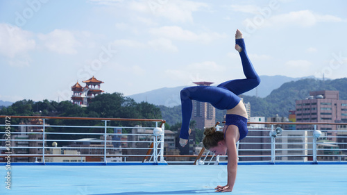 Beautiful flexible girl professional circus acrobat performer handstand, gymnastic bridge, backbend position, graceful woman on cruise liner, sports model on blue background, ship, Asian temple, city