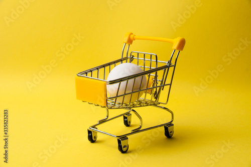 One chicken egg in grocery cart on a yellow background