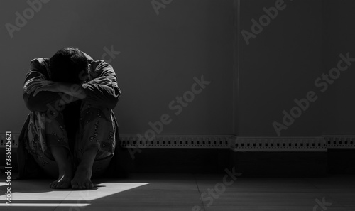 Sunlight and shadow on surface of hopeless man sitting alone with hugging his knees on the floor in empty dark room in black and white style