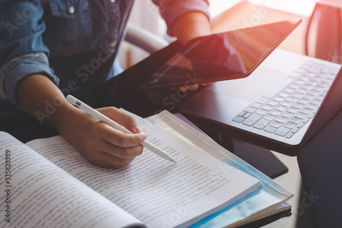 Young woman using digital tablet and work on laptop computer while reading book at home. Online education concept.