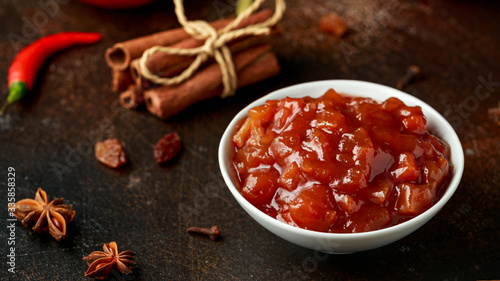 Homemade apple and chilli chutney with spices on dark background