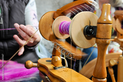 A woman spins wool using a traditional spinning wheel.