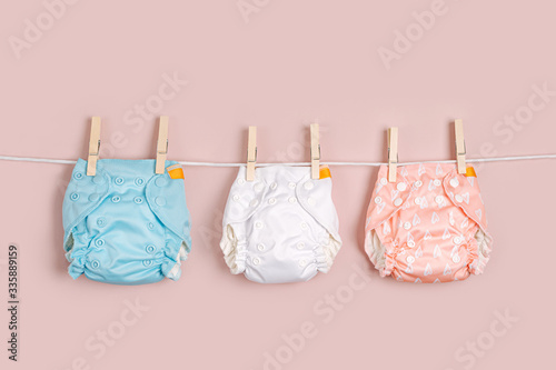 Reusable cloth baby diapers drying on a clothes line. Eco friendly cloth nappies on a pink background. Sustainable lifestyle. Zero waste concept.