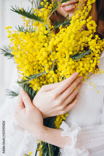 Portrait of a red-haired beautiful girl with a Mimosa in a long white dress