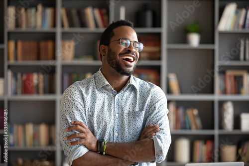 Overjoyed biracial young man in glasses stand laugh talking with friend or colleague, happy excited African American millennial male have fun engaged in pleasant conversation at home or workplace
