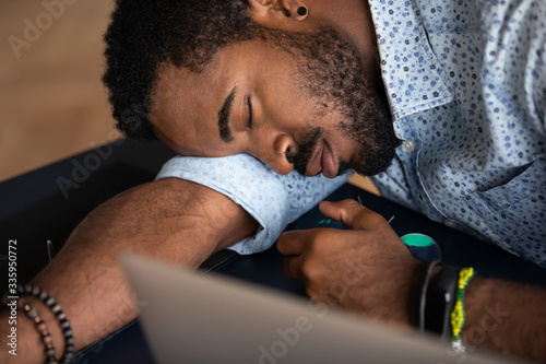 Close up of tired african American male worker or student feel fatigue exhaustion fall asleep at workplace, exhausted biracial man overwhelmed with work take nap sleep at office desk, overwork concept