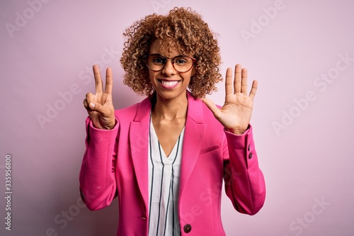 Young african american businesswoman wearing glasses standing over pink background showing and pointing up with fingers number seven while smiling confident and happy.