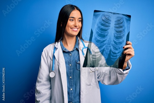 Young beautiful brunette doctor woman wearing stethoscope holding chest xray with a happy face standing and smiling with a confident smile showing teeth