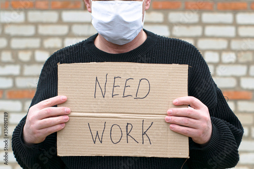 concept unemployment and coronavirus a man in a medical hygienic mask is holding a cardboard tablet with a inscription need work