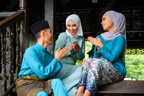 A group of malay muslim people in traditional costume showing greeting gesture during Aidilfitri celebration at terrace of traditional wooden house