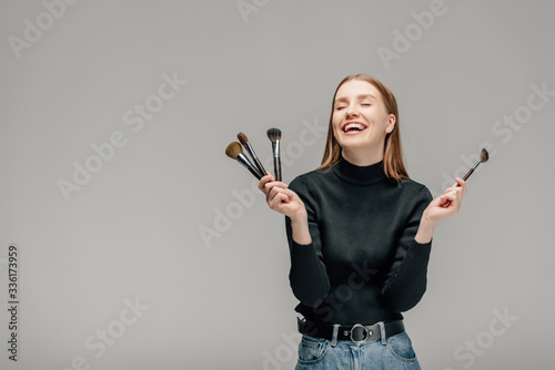 happy makeup artist holding makeup brush set isolated on grey