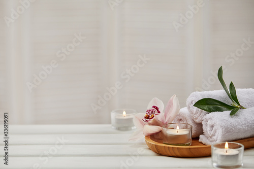 Spa composition with aromatic candles, orchid flower and towel on white wooden table. Beauty spa treatment. copy space