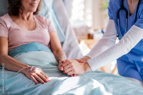 Unrecognizable doctor talking to senior patient in bed in hospital.