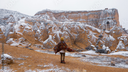 Woman alone with the volcanic landscape at Devrent Valley in Cappadocia. Girl walking around Fairy chimneys surronded by tufa formations at Imaginary Valley in winter season in Cappadocia, Turkey.