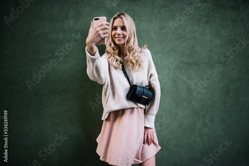 Trendy young woman taking selfie photo by mobile in studio