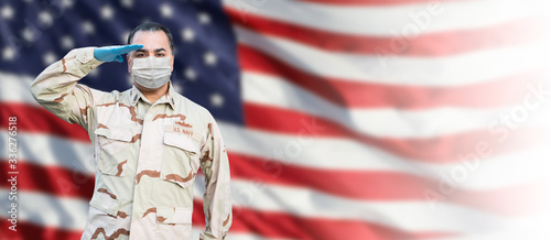 Male Navy Medical Personel Saluting Wearing Personnel Protective Exquipment (PPE) With American Flag Background Banner