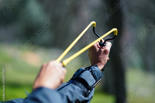 Slingshot aimed and pulled back against wrist, with hands - in forest setting