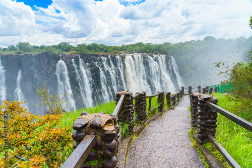 Walking way with view to the dramatic clouds and waterfall at Victoria Falls on the Zambezi River, Zimbabwe, Zambia.