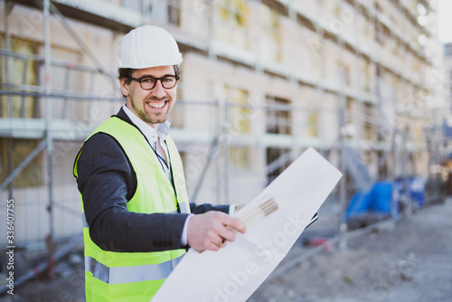 Freudig lächelnder Architekt auf der Baustelle mit Bauplänen 