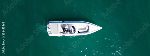 Aerial drone top down ultra wide photo of white speedboat cruise in low speed in emerald clear water lake