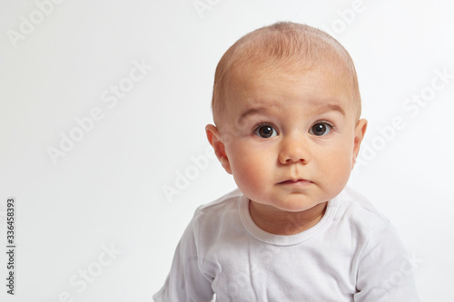 A baby boy looks into camera wearing a white shirt on a white background