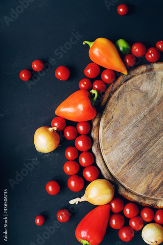 Mix of colorful raw fresh cherry tomatoes, pepper and onion on dark stone table and empty old wooden board