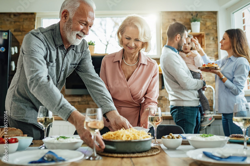 Happy senior couple serving food at dining table while preparing for family lunch.