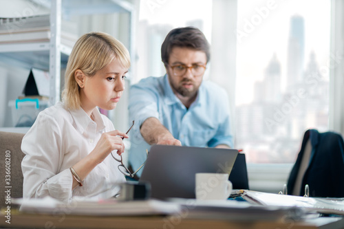 Kind manager giving feedback to young female intern in a busy downtown office. New employee asking for guidance on current project.