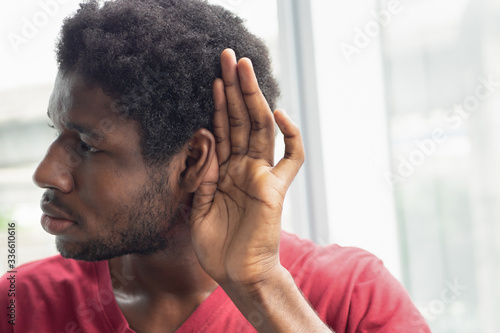 sad frustrated unhappy African black man listening ear to bad news or having hearing impair, hard of hearing; Concept of ear medication, hearing aid, rumor, fake news; African black man model